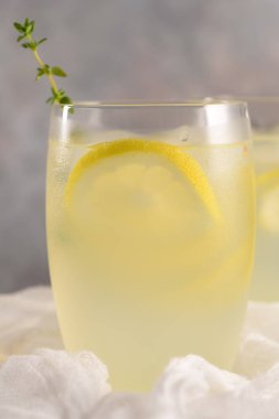 Soğuk limonata veya alkollü kokteyl limon, biberiye ve hafif bir arka plan üzerinde cam bardaklarda buz ile.