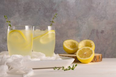 Soğuk limonata veya alkollü kokteyl limon, biberiye ve hafif bir arka plan üzerinde cam bardaklarda buz ile.