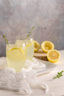 Soğuk limonata veya alkollü kokteyl limon, biberiye ve hafif bir arka plan üzerinde cam bardaklarda buz ile.