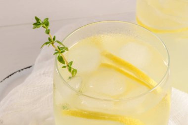 Soğuk limonata veya alkollü kokteyl limon, biberiye ve hafif bir arka plan üzerinde cam bardaklarda buz ile.