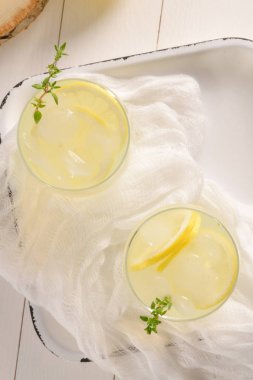 Soğuk limonata veya alkollü kokteyl limon, biberiye ve hafif bir arka plan üzerinde cam bardaklarda buz ile.