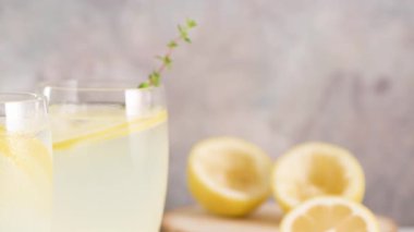 Soğuk limonata veya alkollü kokteyl limon, biberiye ve hafif bir arka plan üzerinde cam bardaklarda buz ile.