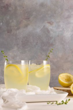 Soğuk limonata veya alkollü kokteyl limon, biberiye ve hafif bir arka plan üzerinde cam bardaklarda buz ile.