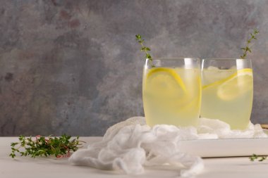 Soğuk limonata veya alkollü kokteyl limon, biberiye ve hafif bir arka plan üzerinde cam bardaklarda buz ile.