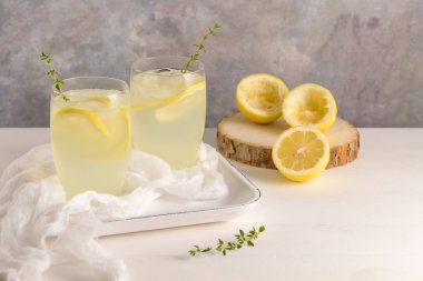 Soğuk limonata veya alkollü kokteyl limon, biberiye ve hafif bir arka plan üzerinde cam bardaklarda buz ile.