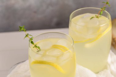 Soğuk limonata veya alkollü kokteyl limon, biberiye ve hafif bir arka plan üzerinde cam bardaklarda buz ile.