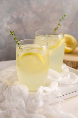 Soğuk limonata veya alkollü kokteyl limon, biberiye ve hafif bir arka plan üzerinde cam bardaklarda buz ile.