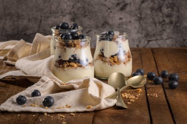 Yaban mersini ve granola yoğurt parfe. Sağlıklı kahvaltı kavramı mason kavanoza ahşap masa üzerinde dekoratif kaşık ile devam eder.
