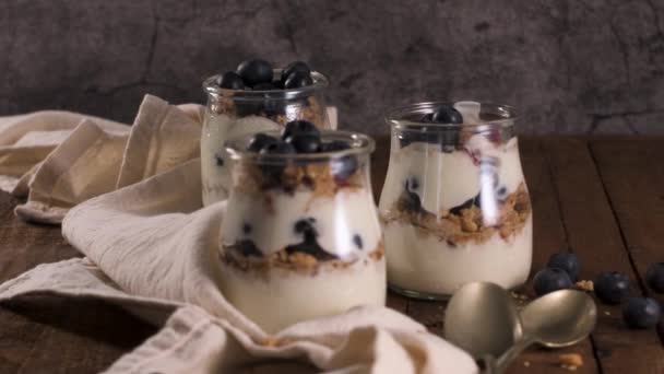 酸奶糕蓝莓和燕麦 健康早餐概念在梅森罐子用装饰勺子在木桌上服务 — 图库视频影像