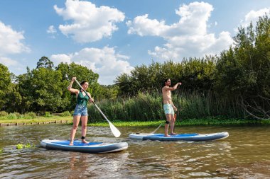 Erkek ve kadın paddleboarding göl kenarında ayağa kalk. Genç çift su sporları göl kenarında yapıyoruz. Yaz tatili sırasında erkek ve kadın turist.