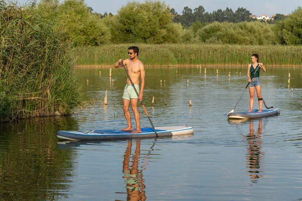 Erkek ve kadın paddleboarding göl kenarında ayağa kalk. Genç çift su sporları göl kenarında yapıyoruz. Yaz tatili sırasında erkek ve kadın turist.