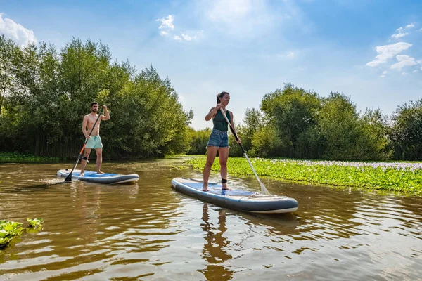 Erkek ve kadın paddleboarding göl kenarında ayağa kalk. Genç çift su sporları göl kenarında yapıyoruz. Yaz tatili sırasında erkek ve kadın turist.