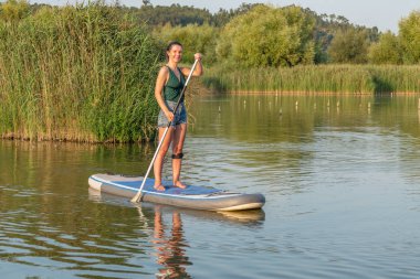 Kadın paddleboarding göl kenarında ayakta. Genç kız gölde su sporları yapıyor. Mayo yaz tatili sırasında kadın turist.