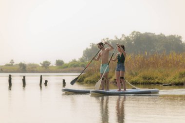 Erkek ve kadın paddleboarding göl kenarında ayağa kalk. Genç çift su sporları göl kenarında yapıyoruz. Yaz tatili sırasında erkek ve kadın turist.