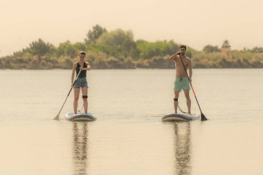 Erkek ve kadın paddleboarding göl kenarında ayağa kalk. Genç çift su sporları göl kenarında yapıyoruz. Yaz tatili sırasında erkek ve kadın turist.