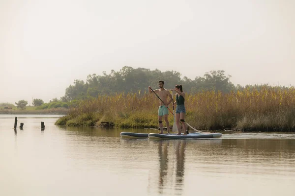 男人和女人站在湖上 Paddleboarding 年轻夫妇正在湖边做水上运动 女游客在暑假期间的旅行 — 图库照片