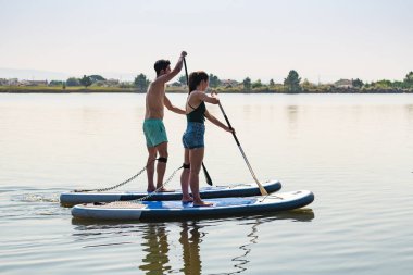 Erkek ve kadın paddleboarding göl kenarında ayağa kalk. Genç çift su sporları göl kenarında yapıyoruz. Yaz tatili sırasında erkek ve kadın turist.