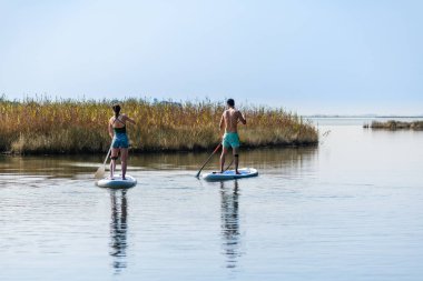 Erkek ve kadın paddleboarding göl kenarında ayağa kalk. Genç çift su sporları göl kenarında yapıyoruz. Yaz tatili sırasında erkek ve kadın turist.