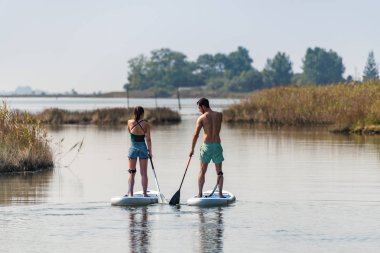 Erkek ve kadın paddleboarding göl kenarında ayağa kalk. Genç çift su sporları göl kenarında yapıyoruz. Yaz tatili sırasında erkek ve kadın turist.