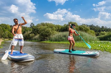 Erkek ve kadın paddleboarding göl kenarında ayağa kalk. Genç çift su sporları göl kenarında yapıyoruz. Yaz tatili sırasında erkek ve kadın turist.