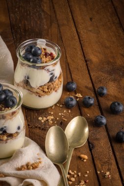 Yaban mersini ve granola yoğurt parfe. Sağlıklı kahvaltı kavramı mason kavanoza ahşap masa üzerinde dekoratif kaşık ile devam eder.