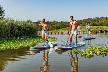 Adam ve kadın paddleboarding göl kenarında ayağa kalk. Göl kenarında su sporları. Yaz tatili sırasında erkek ve kadın turist.