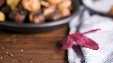 Rustik ahşap tahta ve gri ahşap arka plan, seçici odak üzerinde kavrulmuş kestane dökme demir tava.