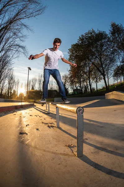 Kaykaycı bir tahta üzerinde slayt yerel skatepark, gün batımında.
