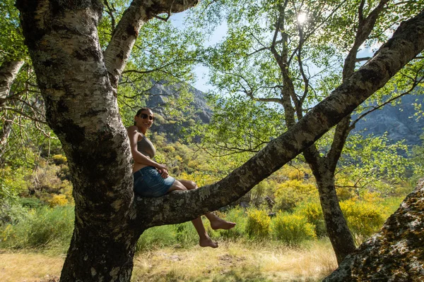 Jonge vrouw glimlachend zittend op de tak van een boom — Stockfoto