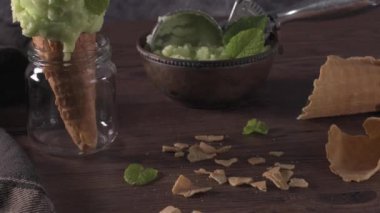 Koyu rustik bir kapta antep fıstığı dondurma ve kahverengi ahşap arka plan üzerinde waffle konisi.