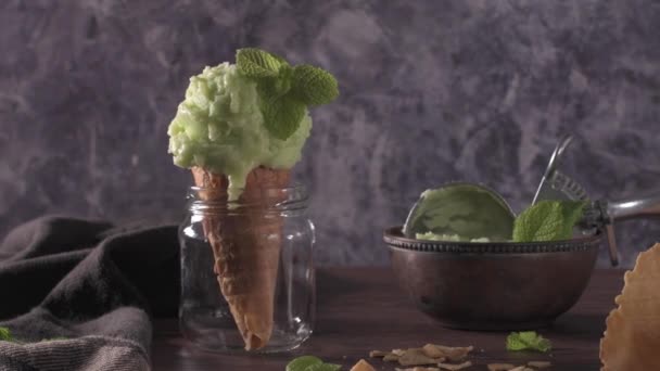 茶色の木製の背景に暗い素朴なボウルとワッフルコーンのピスタチオアイスクリーム — ストック動画