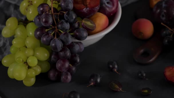 フルーツ白いセラミックボウルに果物と静物 コンクリートの壁ドラマチックな光ブドウ アプリコット プラム — ストック動画