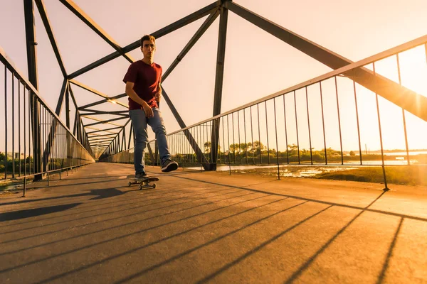 Jonge skateboarder op brug bij zonsondergang — Stockfoto