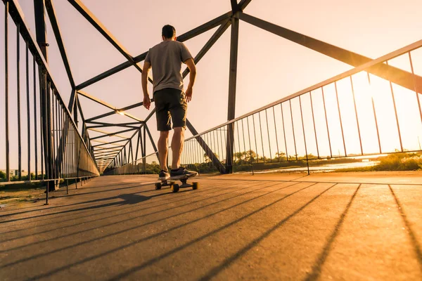 Nuori rullalautailija sillalla auringonlaskun aikaan — kuvapankkivalokuva