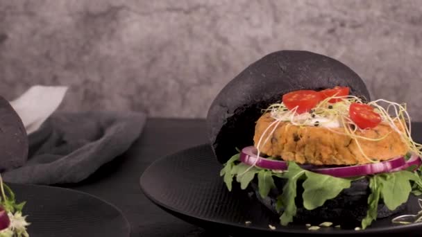 在深色木制台面的黑面包上放有鹰嘴豆和蔬菜的美味烤蔬菜汉堡 — 图库视频影像