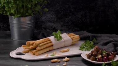 Taze pişmiş ev yapımı Grissini ekmek çubukları beyaz seramik tepside ve mutfak tezgahının üzerinde zeytinyağı ve fesleğen otu ile.
