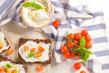 Krem peynirli çavdar ekmeği, zeytinyağı ve fesleğen sosu, kiraz domatesleri, ahşap tahtada taze fesleğen yaprakları..