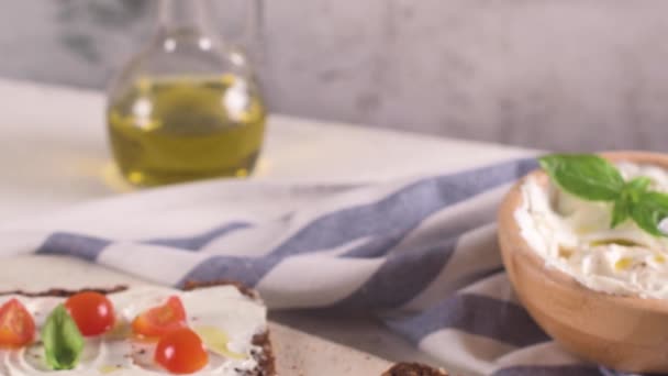 クリームチーズ オリーブオイルとバジルディップ チェリートマト 木製ボード上の新鮮なバジルの葉とライ麦パンブルスケッタ — ストック動画