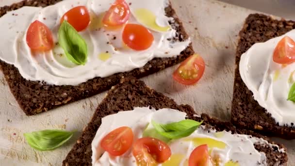 带有奶油奶酪 橄榄油和罗勒酱 樱桃西红柿 木制木板上新鲜罗勒叶的黑麦面包 — 图库视频影像