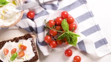 Krem peynirli çavdar ekmeği, zeytinyağı ve fesleğen sosu, kiraz domatesleri, ahşap tahtada taze fesleğen yaprakları..