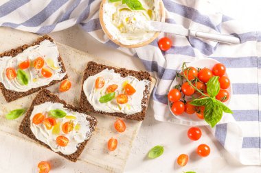 Krem peynirli çavdar ekmeği, zeytinyağı ve fesleğen sosu, kiraz domatesleri, ahşap tahtada taze fesleğen yaprakları..