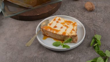 Tek bir dilim karamelli molotof pudingi, tatlı karamel serpiştirilmiş ve taze nane yapraklarıyla süslenmiş, küçük bir kaşıkla tadını çıkarmaya hazır..