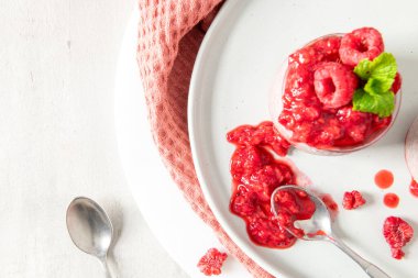 Beyaz bir tabakta tek bir kavanoz ahududu chia tohumu pudinginin yakın çekim, yukarıdan aşağı görüntüsü. Odak noktası zengin, ezilmiş ahududu kompostosu ve tabağa dökülen bir kaşık dolusu böğürtlen. Hayat dolu.