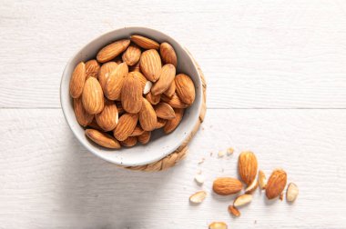 Çiğ bademlerle dolu seramik bir kase beyaz ahşap bir masada dokuma makinesinin üzerinde duruyor..