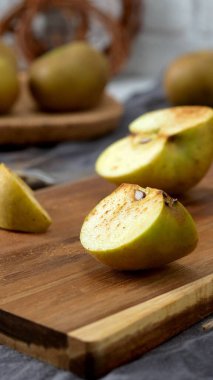 Yarı kesilmiş bir elma ve hafif tarçınlı küçük bir kama, kırsal bir ahşap kesme tahtasının üzerinde sunuluyor. Sahne bir bıçak, sicim ve küçük bir kase tarçınla hazırlandı. Bu da lezzetli bir atıştırmalık için samimi ve sonbahar hazırlığı olduğunu gösteriyor.. 