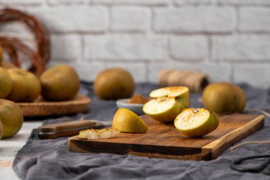 Samimi bir hayat, beyaz ahşap bir masada elma hazırlama sahnesini yakalar. Dilimlenmiş yeşil elmalar, hafifçe tarçınla tozlanmış, yakındaki bir bıçakla ahşap bir kesme tahtasına yerleştirilirken, bütün elmalar koyu bir g 'ye saçılmış.
