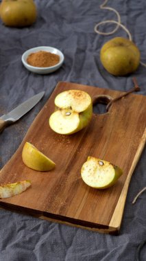 Birkaç altın elma, ahşap bir masa üzerine saçılmış kumaş ve mantar işlemeli kumaş ile. Bıçak ve kesme tahtası dilimlenmiş, tarçın tozlu bir elma sıcak, ev yapımı bir yemek için yakın bir hazırlık olduğunu gösteriyor..