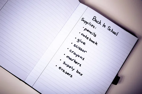 Handwritten shopping list of back to school supplies written on page of a notebook