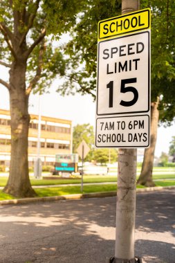 Sign indicating school zone speed limit of 15 miles per hour with school building seen in the background clipart