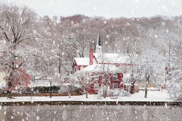 Beautiful rural winter scene with church, trees, pond with falling snow